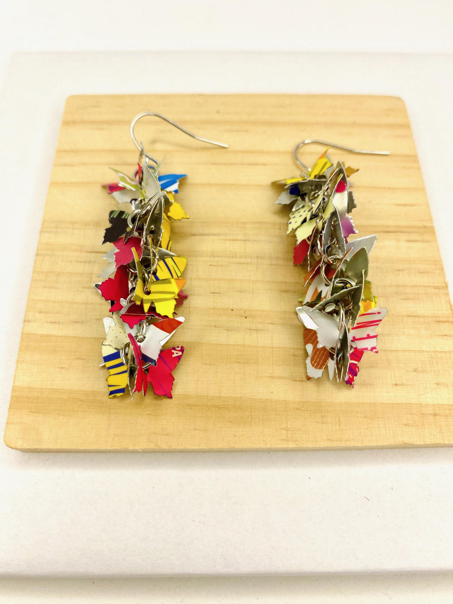 colourful, cascade statement earrings featuring tiny butterflies that are upcycled from craft beer cans on a wooden and white background