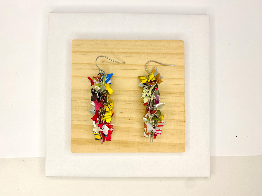 colourful, cascade statement earrings featuring tiny butterflies that are upcycled from craft beer cans on a wooden and white background