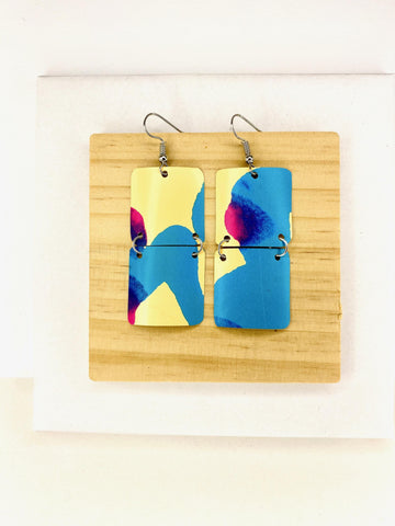 squared shape, abstract, upcycled earrings in blue, yellow, magenta colours made from a craft beer can,  on a wooden background