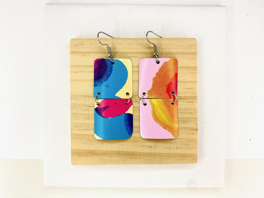 asymmetric, geometric earrings made from upcycled craft beer cans, in blue, yellow, magenta, orange and pink colours on a wooden and white background