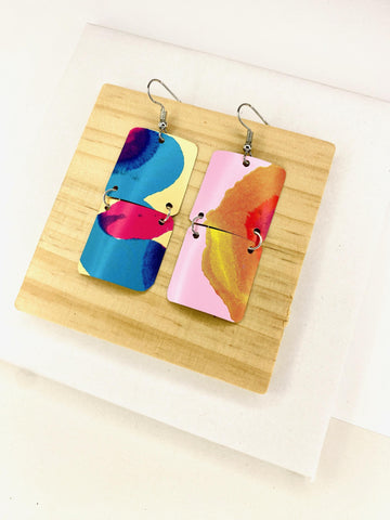 asymmetric, geometric earrings made from upcycled craft beer cans, in blue, yellow, magenta, orange and pink colours on a wooden and white background