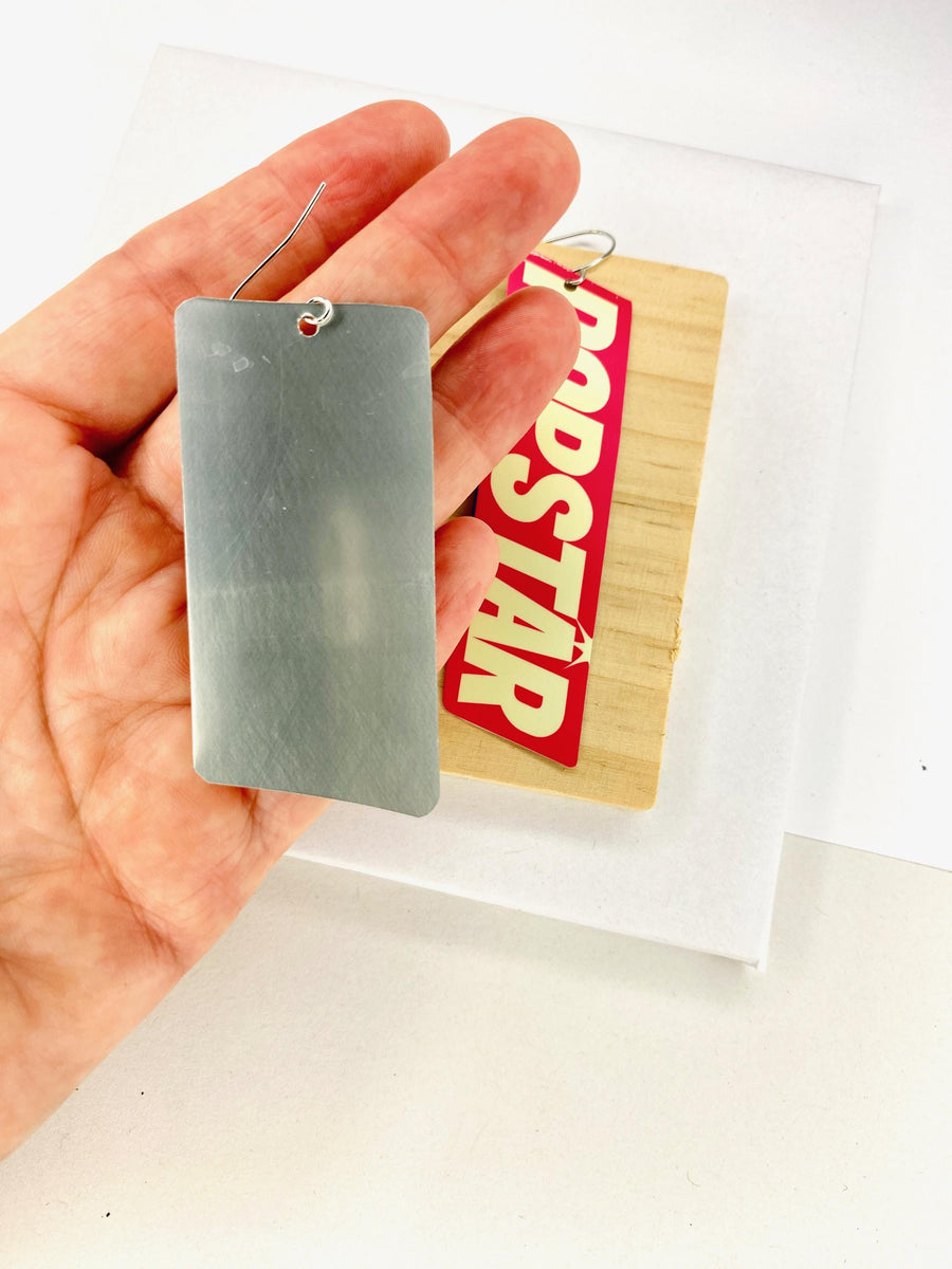 90s, disco, pop-art earrings featuring POPSTAR text and women's face in comic style on a wooden and white background and displayed in hand