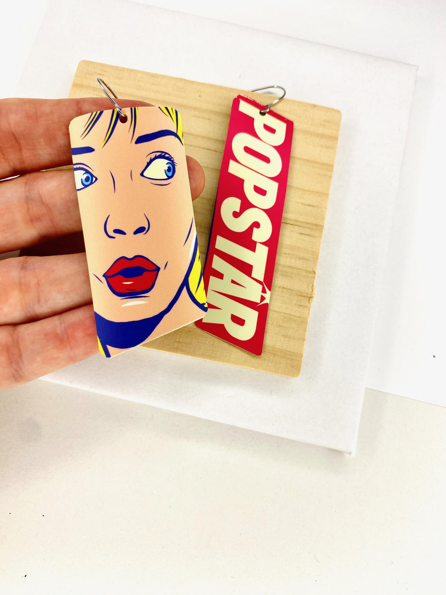 90s, disco, pop-art earrings featuring POPSTAR text and women's face in comic style on a wooden and white background