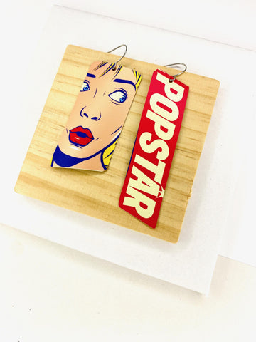 90s, disco, pop-art earrings featuring POPSTAR text and women's face in comic style on a wooden and white background