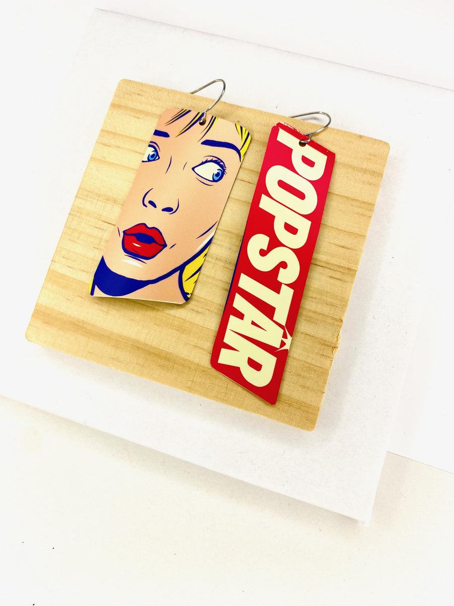90s, disco, pop-art earrings featuring POPSTAR text and women's face in comic style on a wooden and white background
