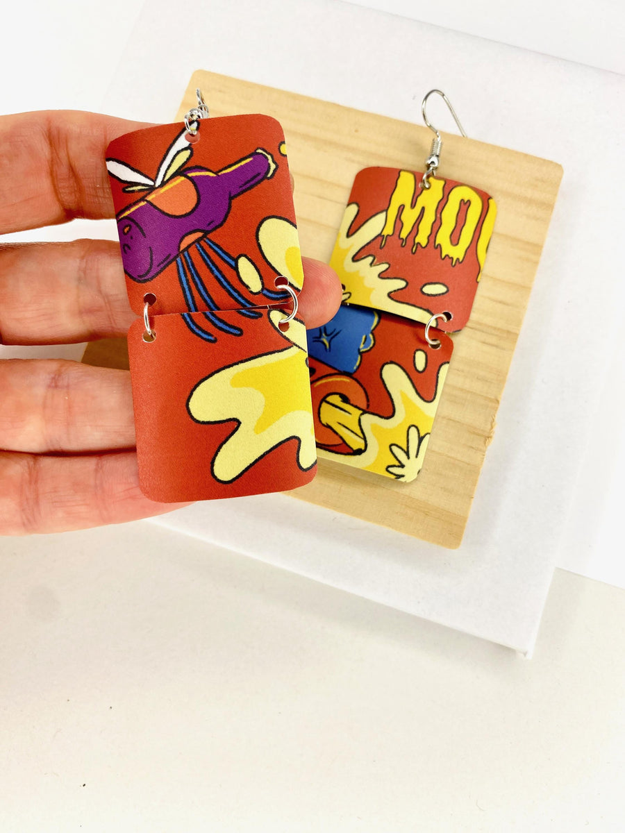 comic, graffiti style earrings made from an upcycled craft beer can in orange, yellow colours, on a wooden and white background