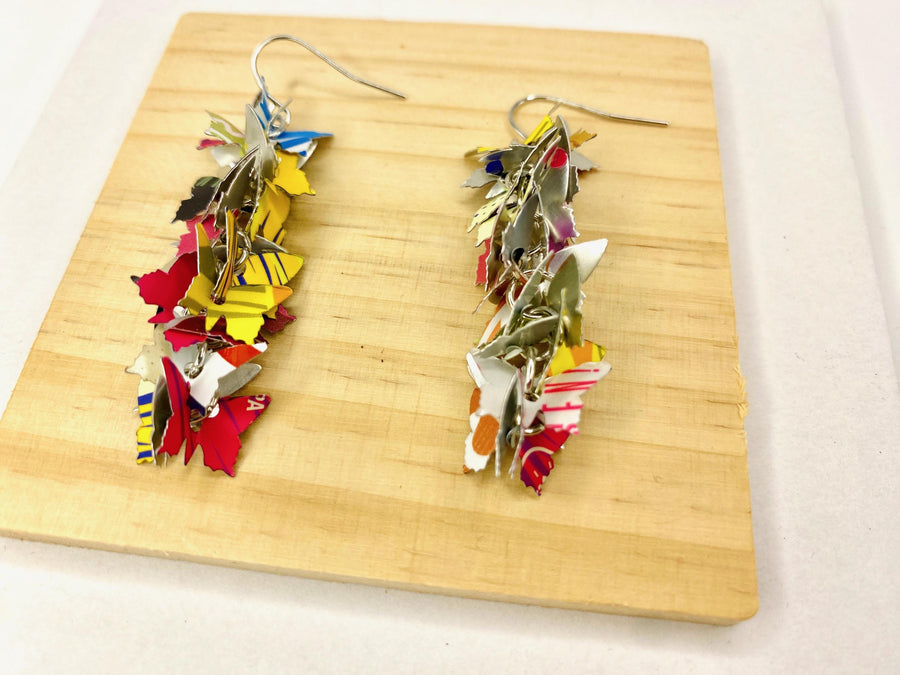 colourful, cascade statement earrings featuring tiny butterflies that are upcycled from craft beer cans on a wooden and white background