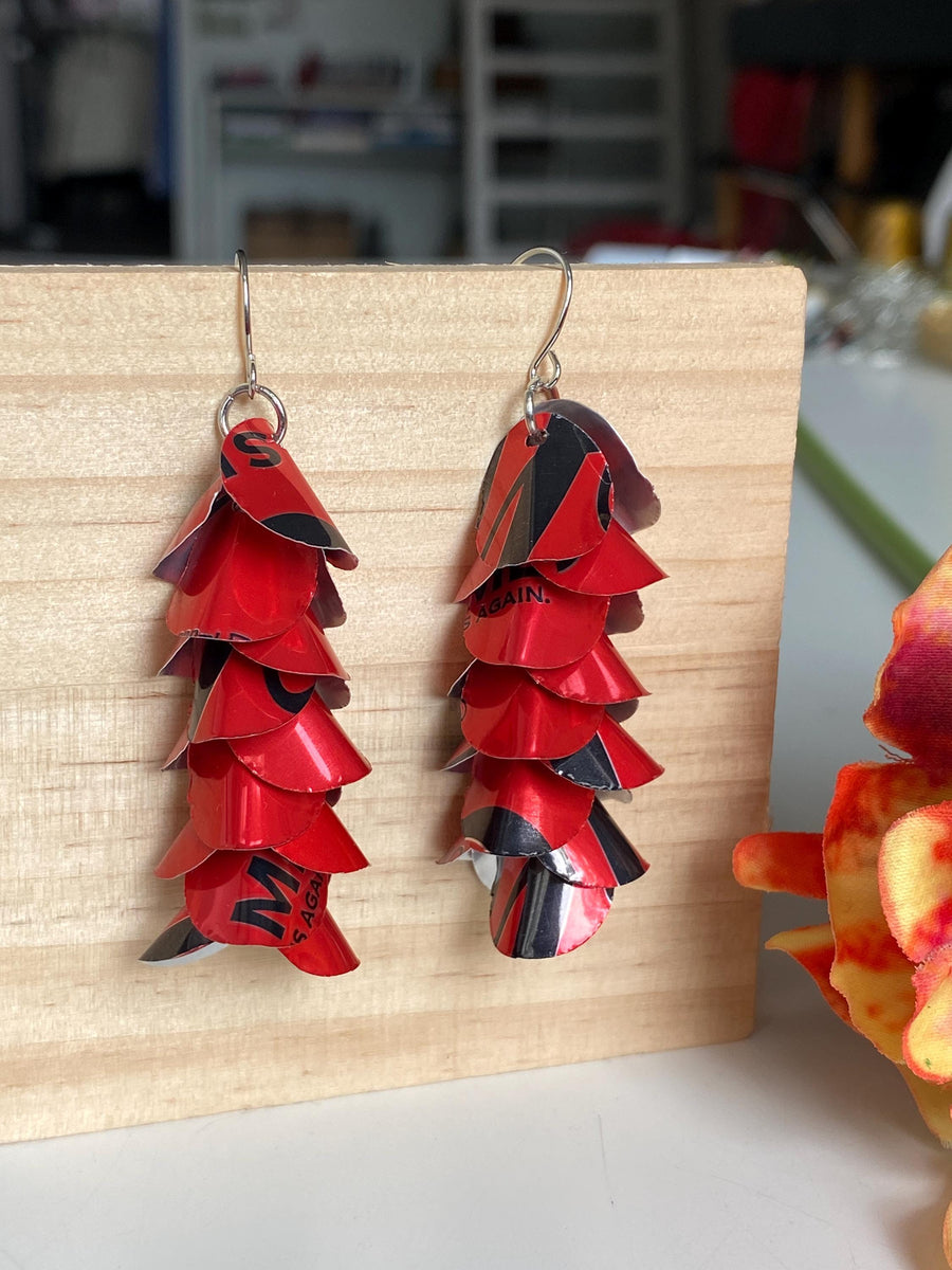 red cascade earrings made from upcycled coca cola aluminum canson a wooden background and flower decoration