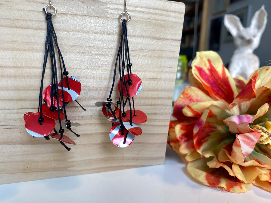 upcycled red black disc earrings on waxed cotton threads, made by Laura Zabo on a wooden background and flower decoration