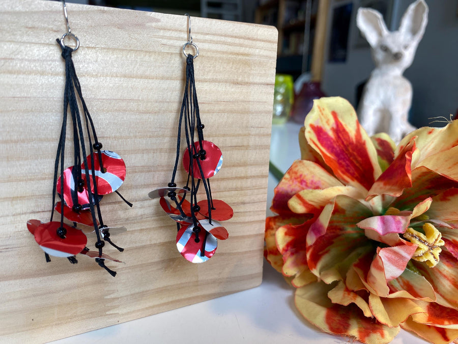 upcycled red black disc earrings on waxed cotton threads, made by Laura Zabo on a wooden background and flower decoration