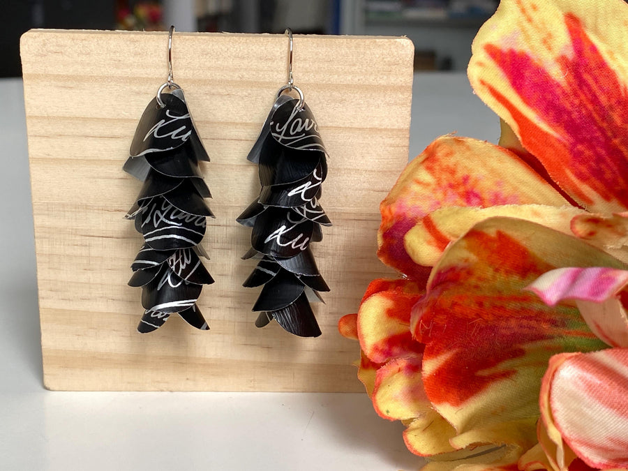 black white cascade earrings made from upcycled lavazza coffee pods by laura zabo, on a wooden background and flower decoration