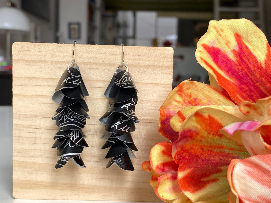 black white cascade earrings made from upcycled lavazza coffee pods by laura zabo, on a wooden background and flower decoration
