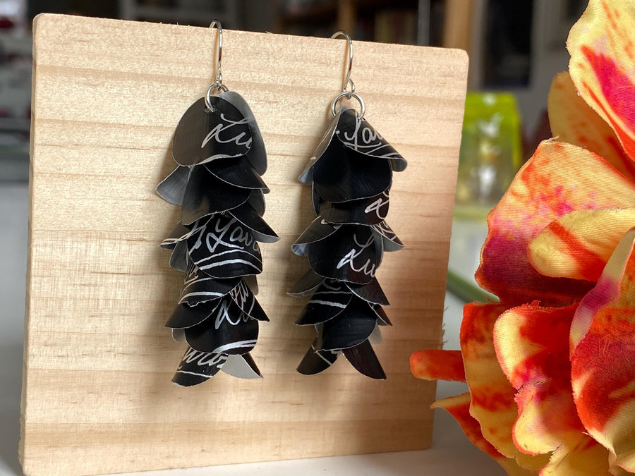 black white cascade earrings made from upcycled lavazza coffee pods by laura zabo, on a wooden background and flower decoration