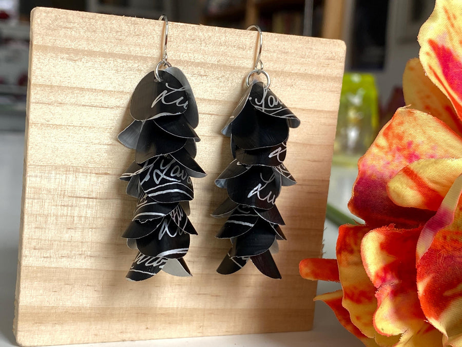black white cascade earrings made from upcycled lavazza coffee pods by laura zabo, on a wooden background and flower decoration