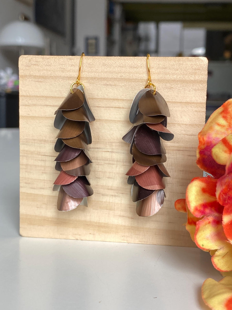 brown coloured cascade earrings made from upcycled nespresso capsules by Laura Zabo, on a wooden background a flower decoration