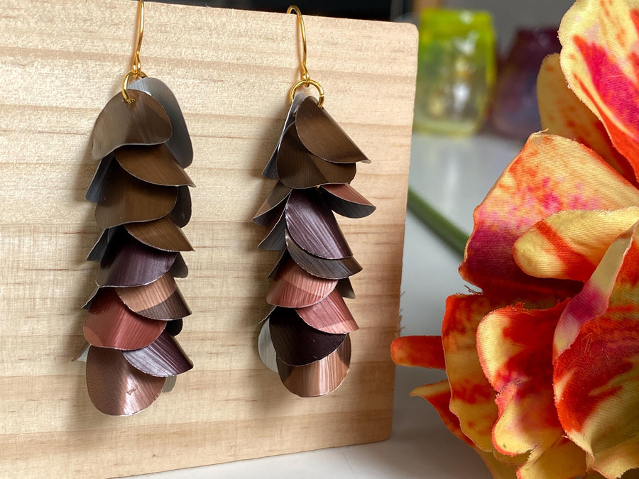 brown coloured cascade earrings made from upcycled nespresso capsules by Laura Zabo, on a wooden background a flower decoration