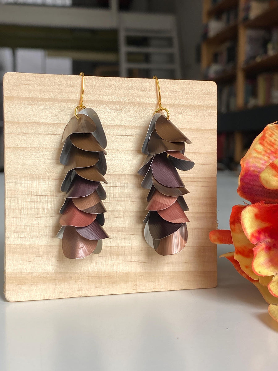 brown coloured cascade earrings made from upcycled nespresso capsules by Laura Zabo, on a wooden background a flower decoration