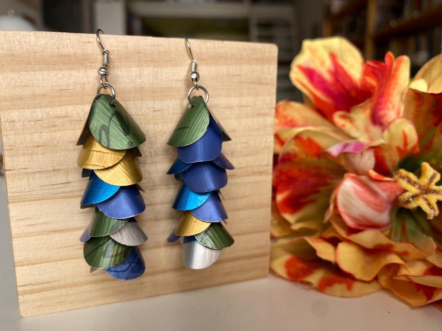 blue green gold silver cascade earrings made from upcycled nespresso capsules by laura zabo on a wooden background and flower decoration