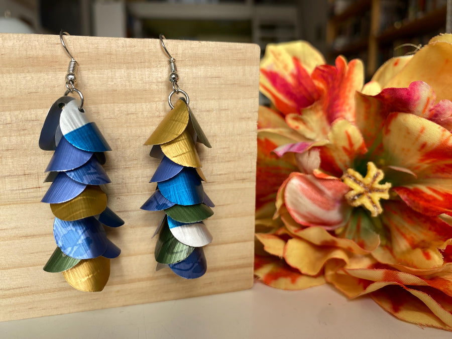 blue green gold silver cascade earrings made from upcycled nespresso capsules by laura zabo on a wooden background and flower decoration