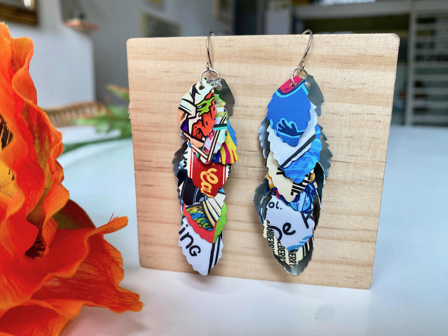colorful, bright, graffiti style cascade earrings made from upcycled craft beer can by laura zabo on a wooden background and flower decoration