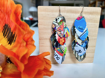 colorful, bright, graffiti style cascade earrings made from upcycled craft beer can by laura zabo on a wooden background and flower decoration