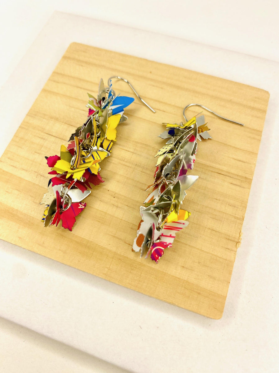 colourful cascade earrings featuring tiny butterfly layers made from upcycled craft beer cans by laura zabo, on a wooden and white background