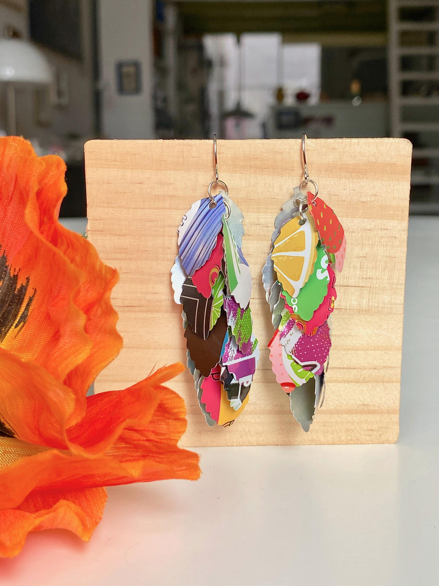 colourful cascade earrings made from craft beer and soda cans by laura zabo on a wooden background and flower decoration