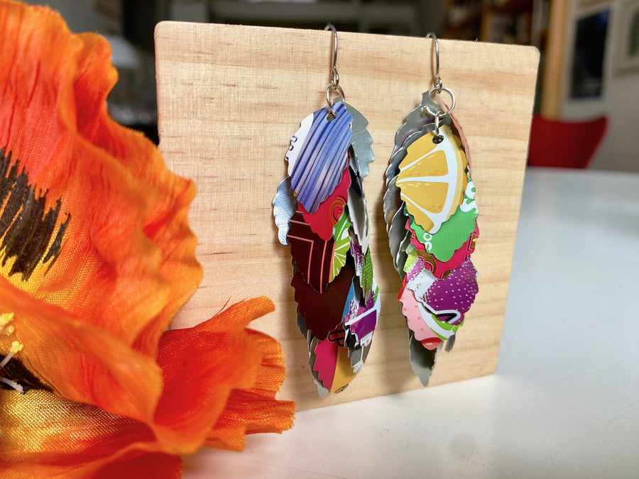 colourful cascade earrings made from craft beer and soda cans by laura zabo on a wooden background and flower decoration
