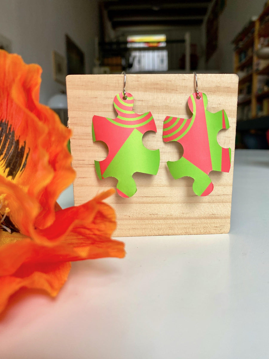puzzle shaped earrings in bright green and peach colour made from upcycled craft beer can by laura zabo on a wooden background and flower decoration