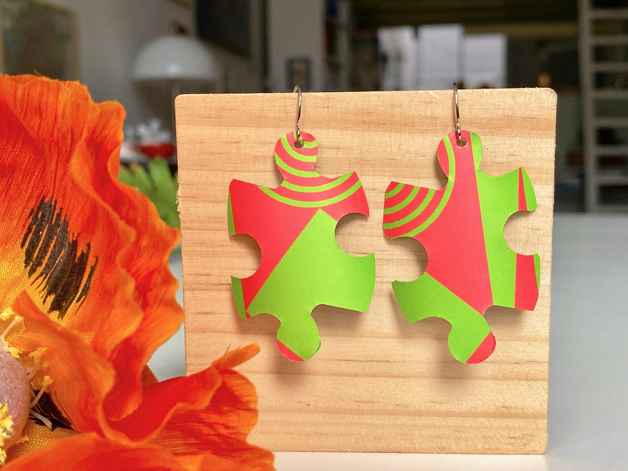 puzzle shaped earrings in bright green and peach colour made from upcycled craft beer can by laura zabo on a wooden background and flower decoration