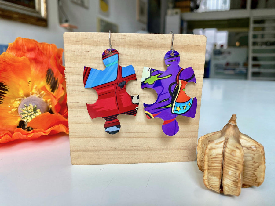 blue purple red graffiti, urban style puzzle shaped earrings made from upcycled beer can by laura zabo on a wooden background and flower decoration