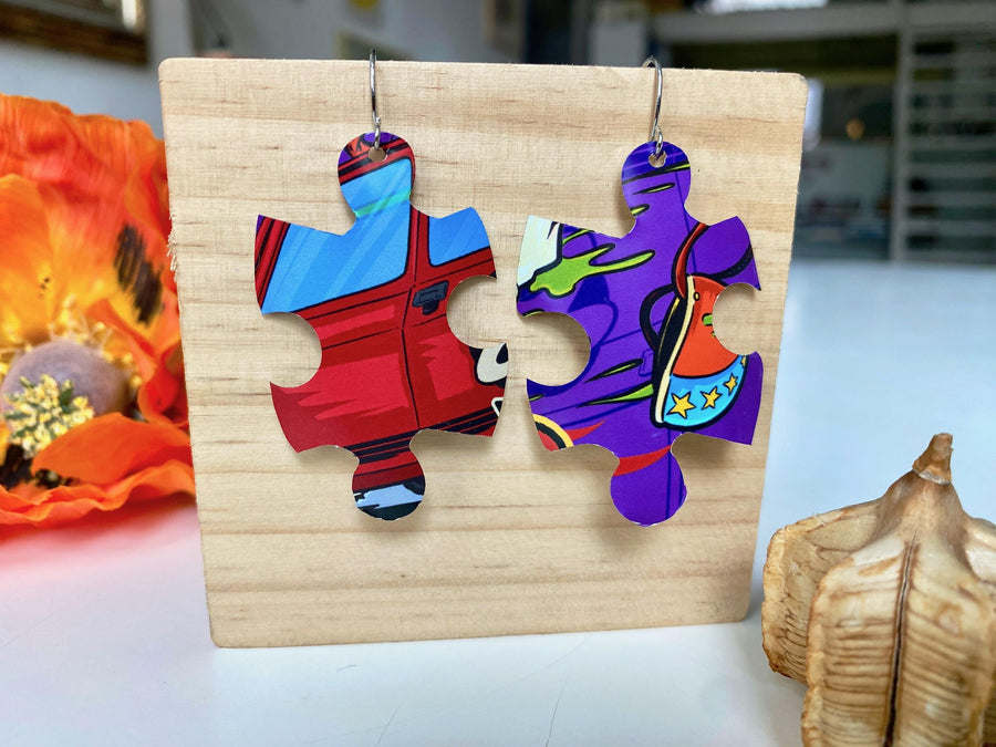 blue purple red graffiti, urban style puzzle shaped earrings made from upcycled beer can by laura zabo on a wooden background and flower decoration