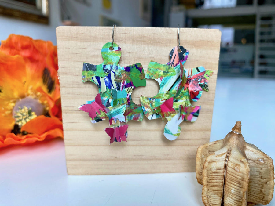 colourful, puzzle shaped earrings adorned with tiny butterflies made from upcycled craft beer cans by laura zabo on a wooden background and flower design