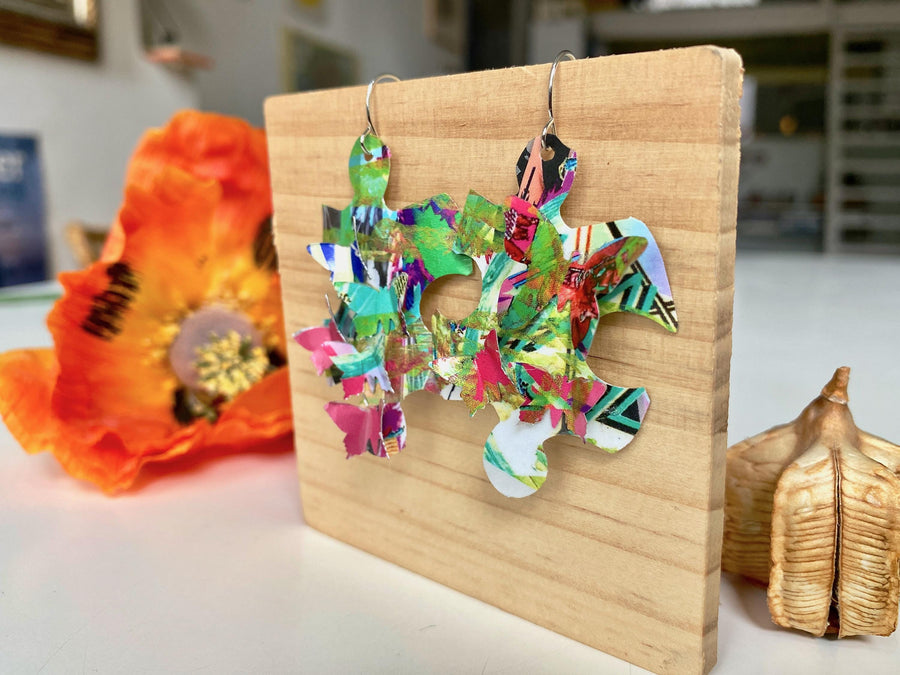 colourful, puzzle shaped earrings adorned with tiny butterflies made from upcycled craft beer cans by laura zabo on a wooden background and flower design