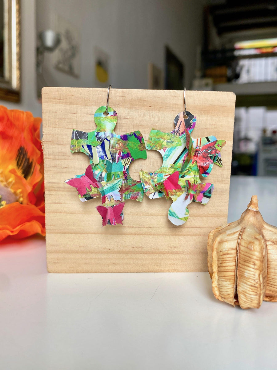 colourful, puzzle shaped earrings adorned with tiny butterflies made from upcycled craft beer cans by laura zabo on a wooden background and flower design