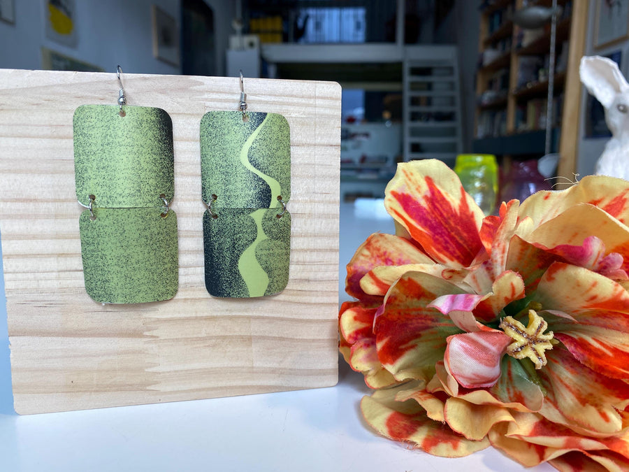 mint green and black retro 90s earrings made from upcycled craft beer can by Laura zabo, on a wooden background and flower decoration