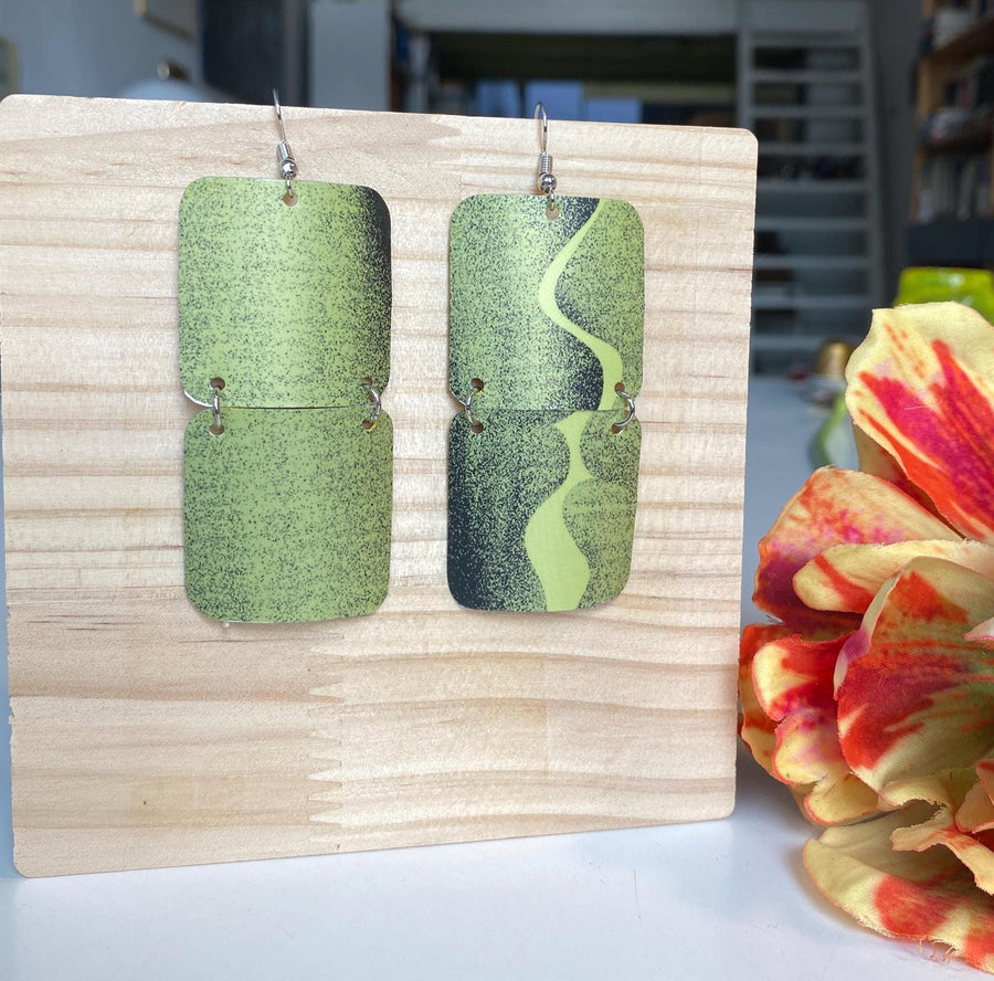 mint green and black retro 90s earrings made from upcycled craft beer can by Laura zabo, on a wooden background and flower decoration