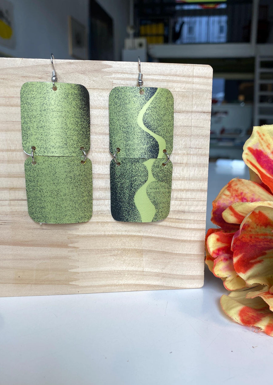 mint green and black retro 90s earrings made from upcycled craft beer can by Laura zabo, on a wooden background and flower decoration