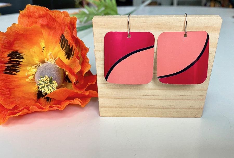 Laura Zabo , dark and light pink squared earrings made from shiny craft beer can, on a wooden background and flower decoration