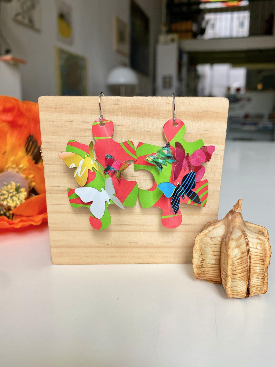Beautiful, bright, multicoloured, puzzle shaped earrings with tiny butterflies, made from upcycled craft beer cans by Laura Zabo on a wooden background