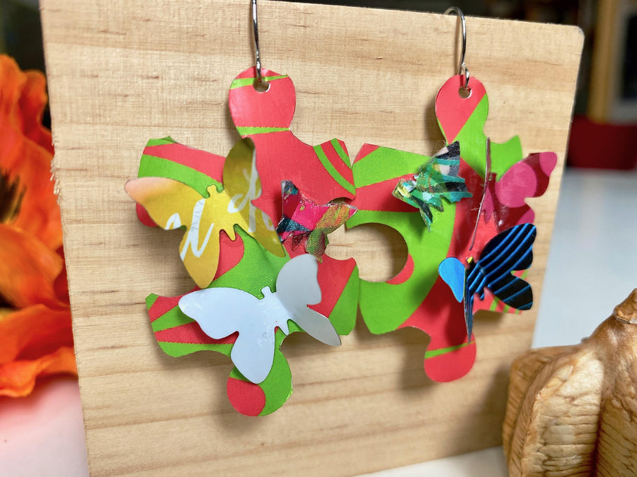 Beautiful, bright, multicoloured, puzzle shaped earrings with tiny butterflies, made from upcycled craft beer cans by Laura Zabo on a wooden background