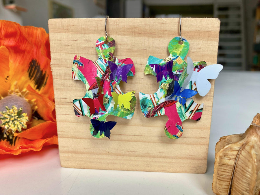multicoloured, bright puzzle shaped earrings with butterflies made from craft beer cans by laura zabo on a wooden background and plant decoration