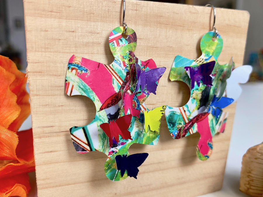 multicoloured, bright puzzle shaped earrings with butterflies made from craft beer cans by laura zabo on a wooden background and plant decoration