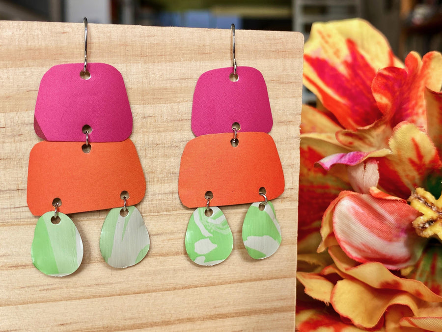 pink orange and green earrings made from upcycled craft beer cans and nespresso capsules by laura zabo on a wooden background and flower decoration