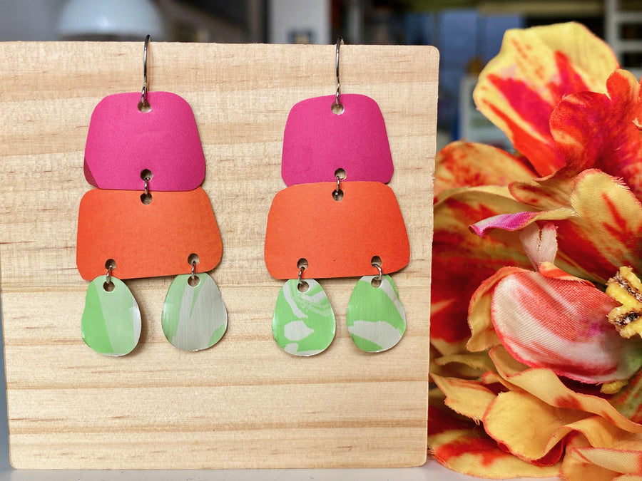 pink orange and green earrings made from upcycled craft beer cans and nespresso capsules by laura zabo on a wooden background and flower decoration