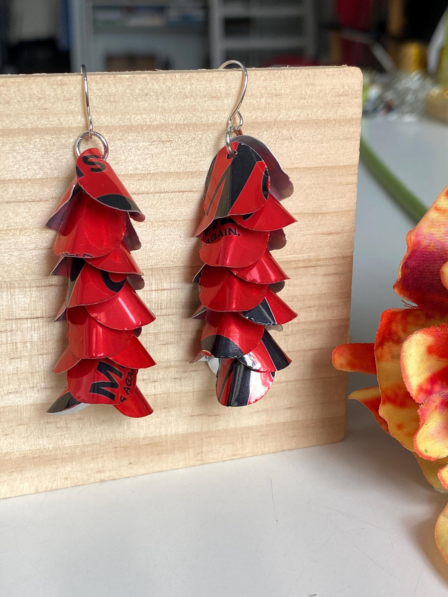 red cascade earrings made from upcycled coca cola aluminum canson a wooden background and flower decoration
