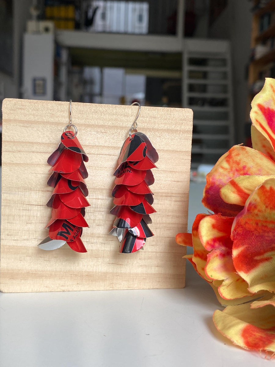 red cascade earrings made from upcycled coca cola aluminum canson a wooden background and flower decoration