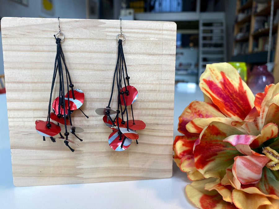upcycled red black disc earrings on waxed cotton threads, made by Laura Zabo on a wooden background and flower decoration