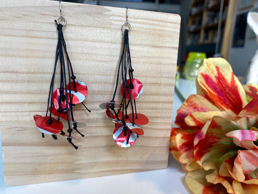 upcycled red black disc earrings on waxed cotton threads, made by Laura Zabo on a wooden background and flower decoration