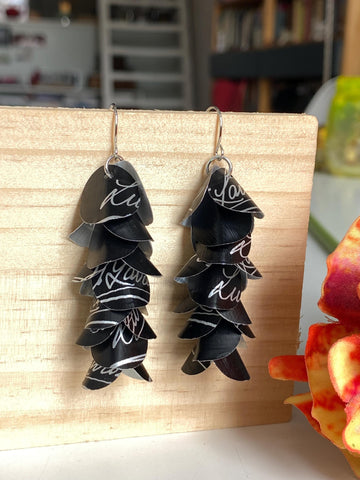 black white cascade earrings made from upcycled lavazza coffee pods by laura zabo, on a wooden background and flower decoration